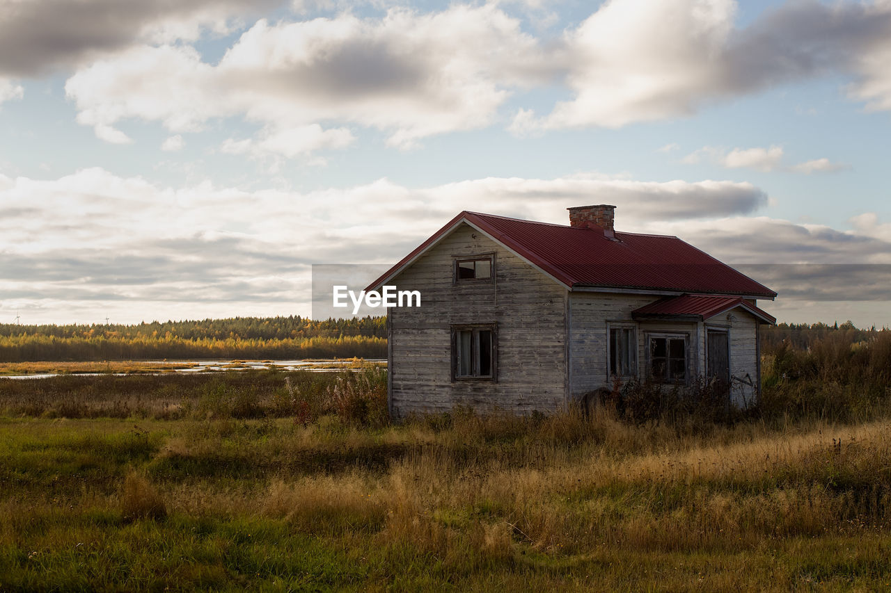 An old abandoned house by a small swamp lake. the windows of the house have been broken.