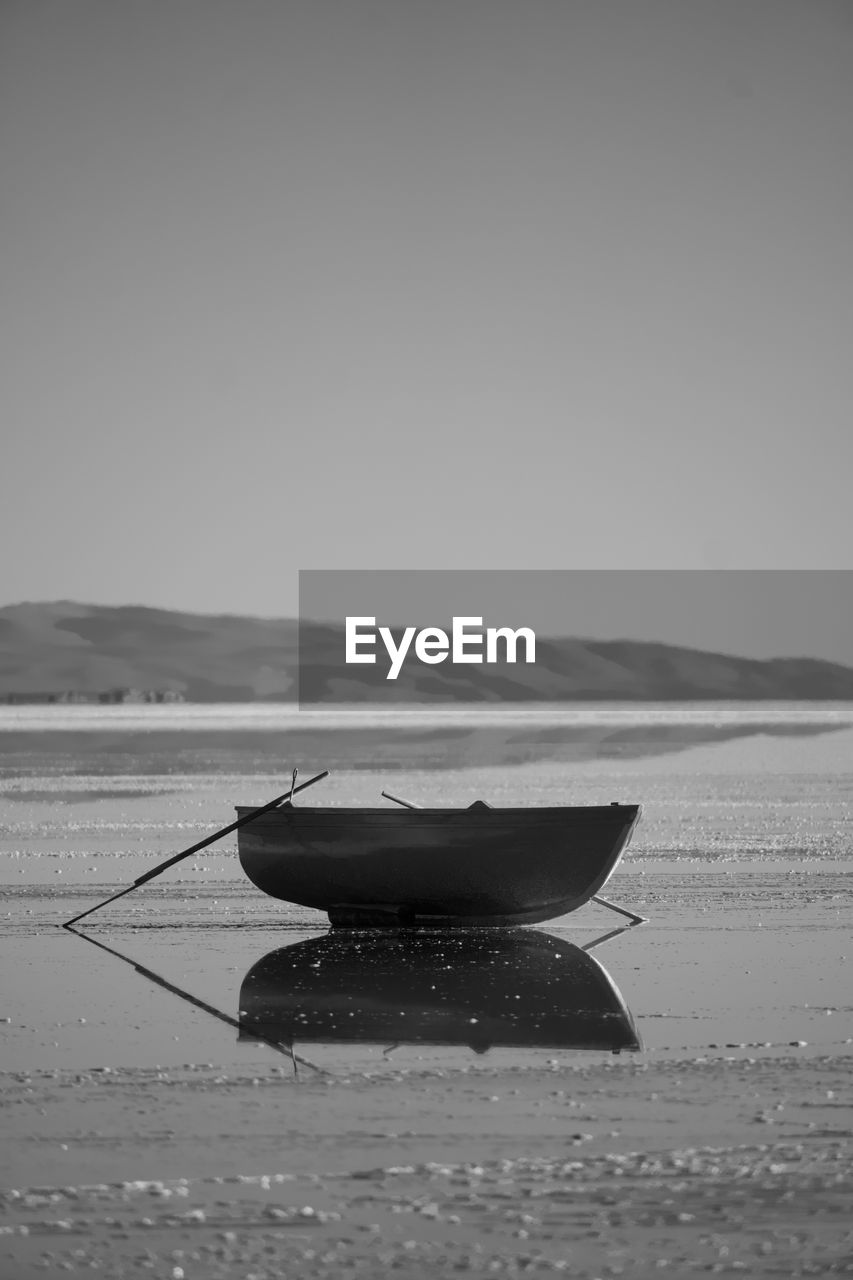 water, black and white, vehicle, monochrome, sea, monochrome photography, nature, sky, nautical vessel, land, tranquility, boat, beauty in nature, wave, beach, transportation, scenics - nature, black, no people, day, clear sky, ocean, outdoors, tranquil scene, reflection, watercraft, horizon, sand, mode of transportation, travel, copy space, shore, environment, non-urban scene
