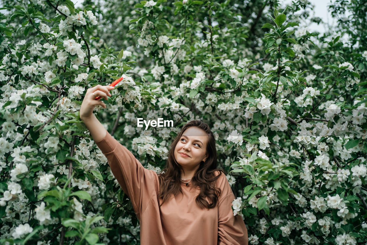 Girl in blooming apple tree using smartphone video call outdoor nature