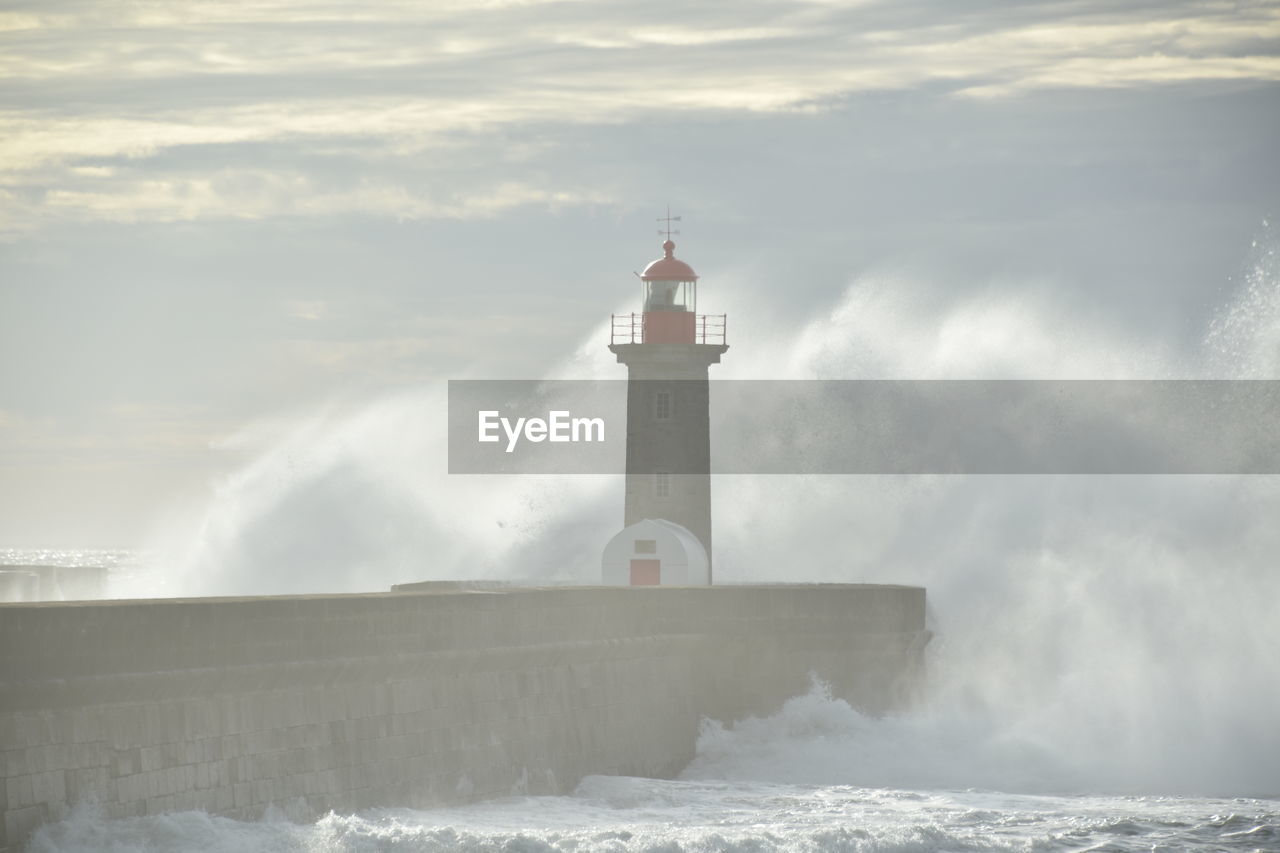 Lighthouse by sea against sky with the big wave