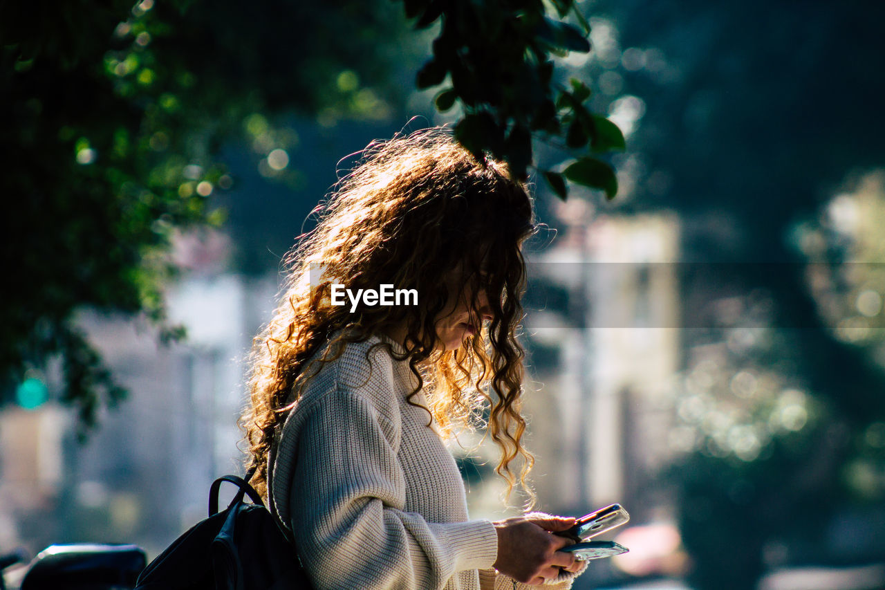 MIDSECTION OF WOMAN USING SMART PHONE WHILE STANDING ON TREE