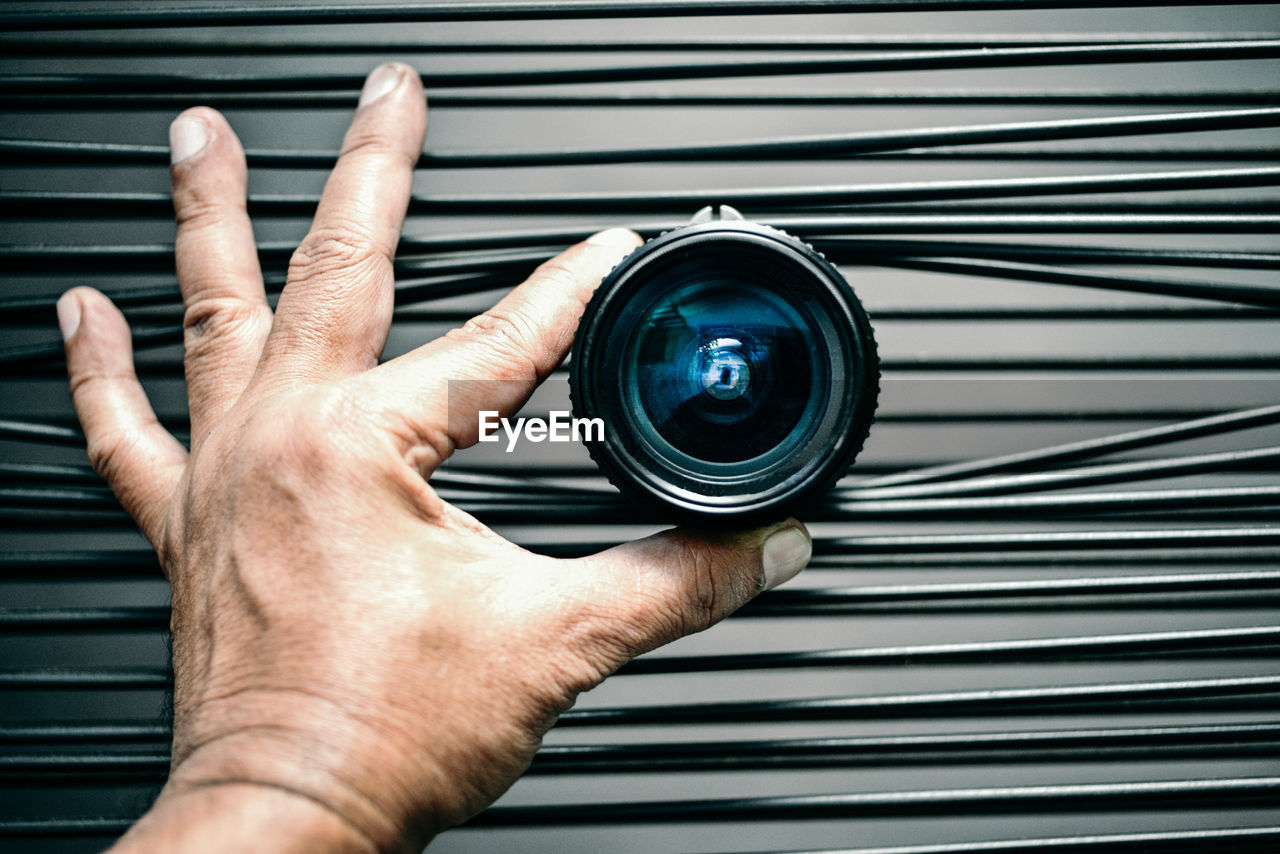 Cropped image of man holding camera lens amidst cables
