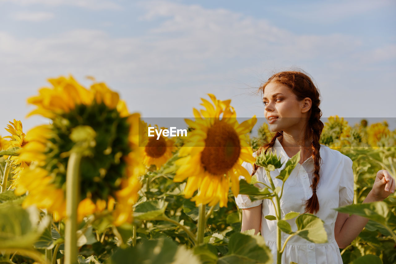 portrait of woman holding yellow flowers against sky