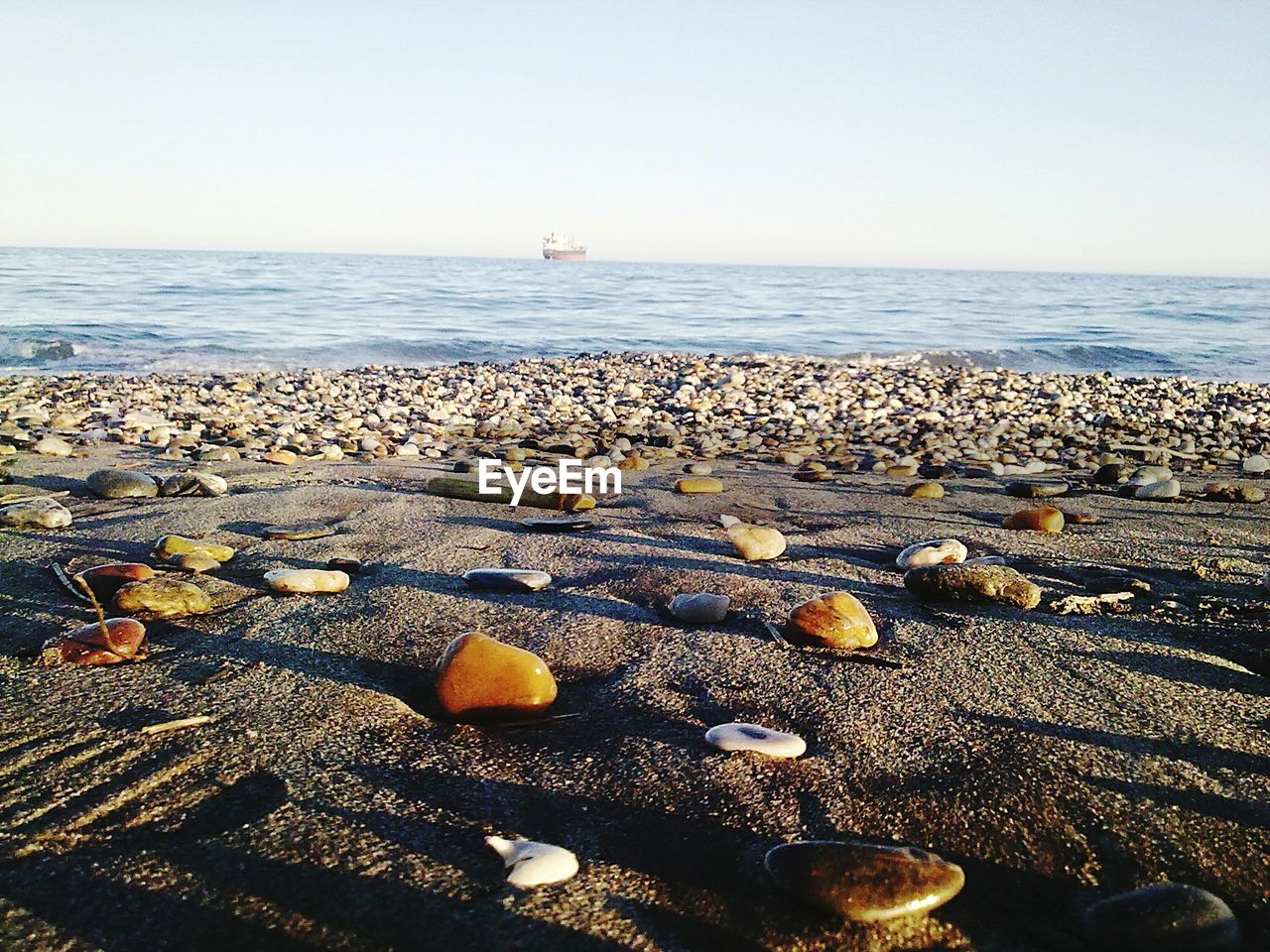 Pebbles on sandy sea shore against clear sky