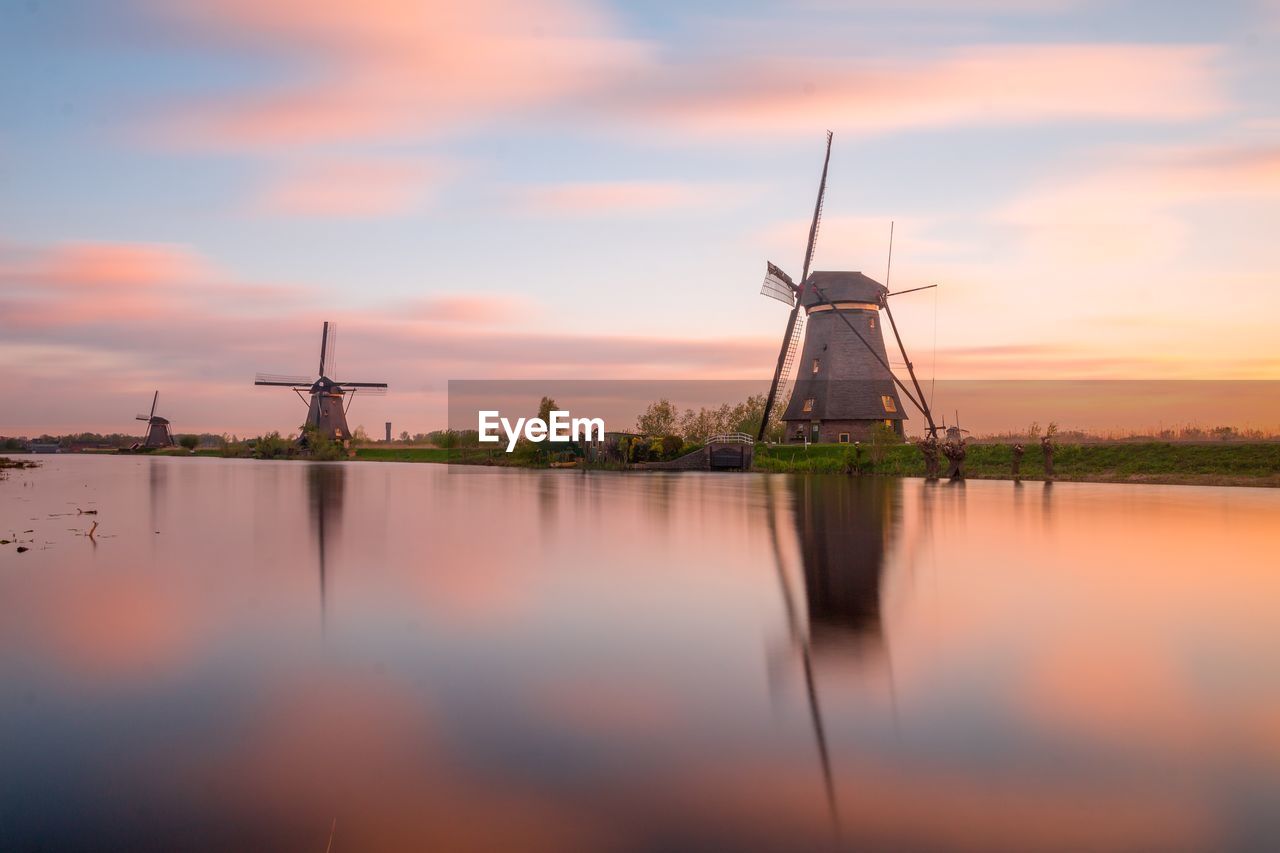 Traditional windmill by lake against sky during sunset