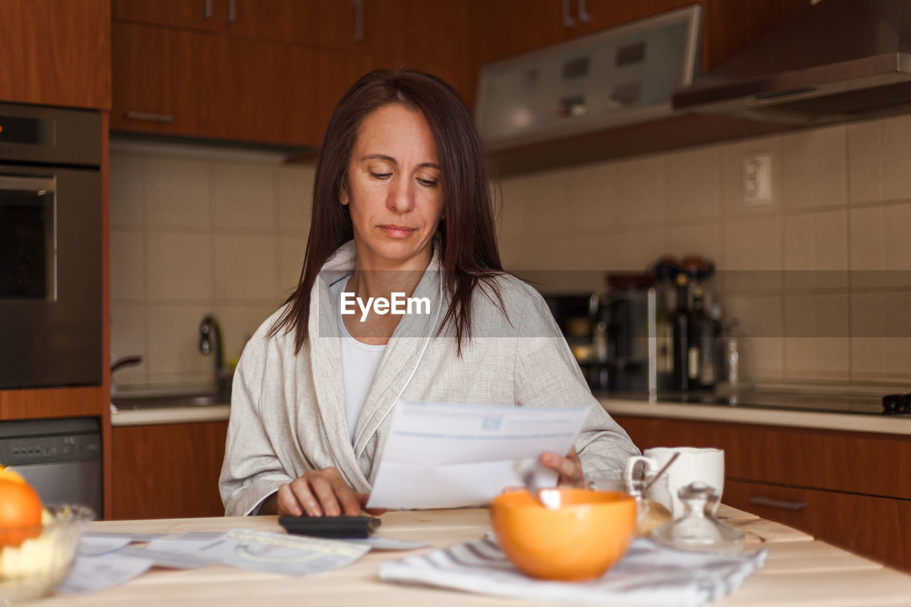Woman reading document while having breakfast at home