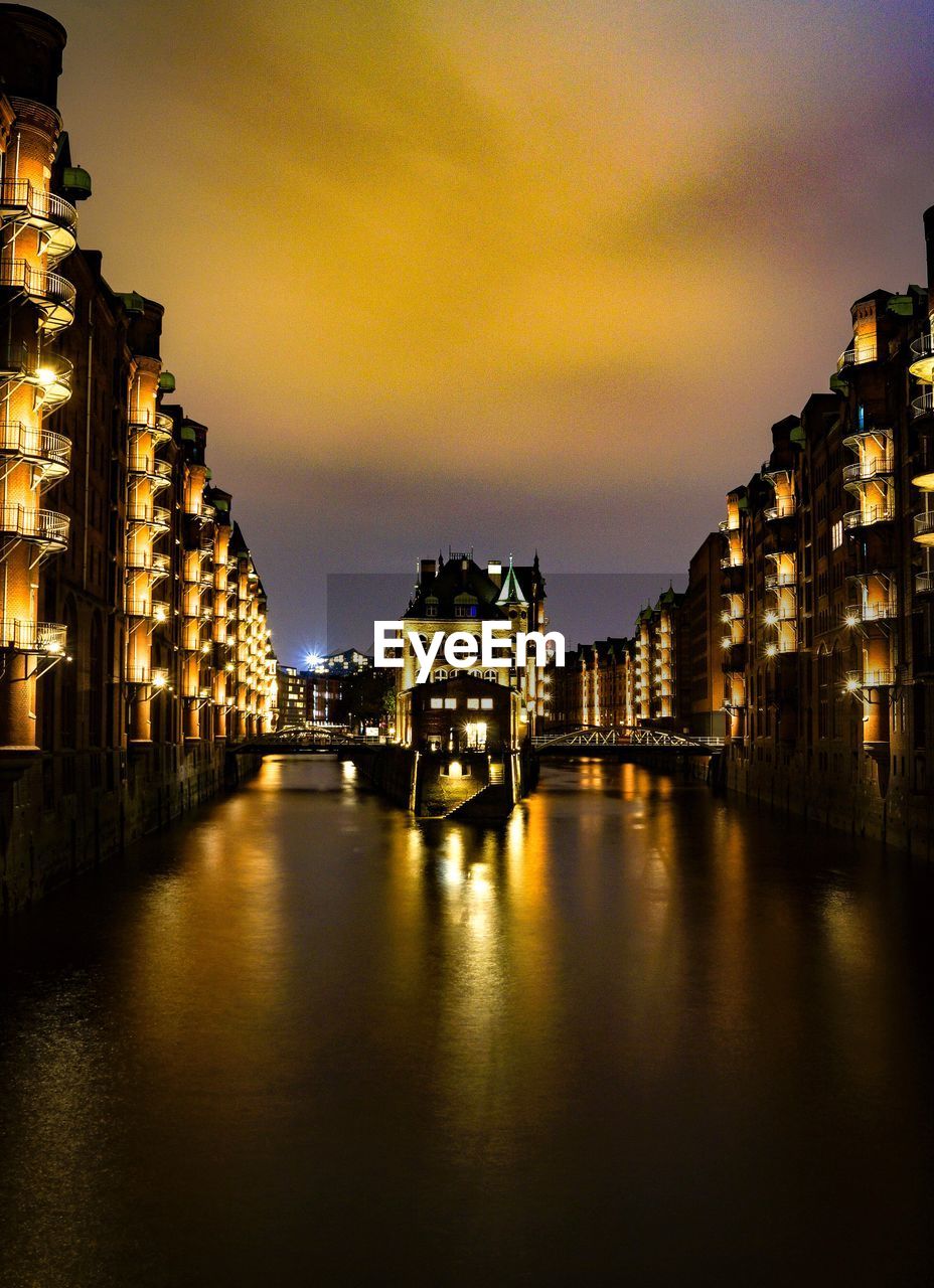 Illuminated buildings by river against sky at night