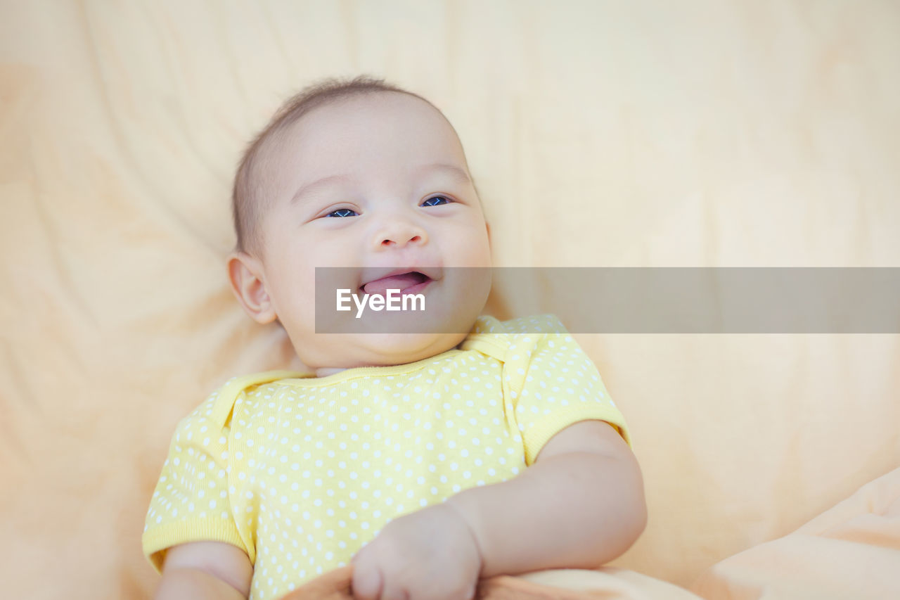 High angle view of cute smiling baby girl lying on bed at home