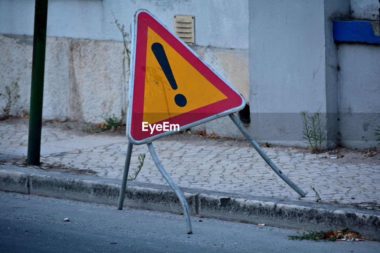 sign, communication, warning sign, road, traffic sign, no people, yellow, road sign, red, day, street, triangle shape, art, city, wall, blue, guidance, outdoors, urban area, signage, architecture