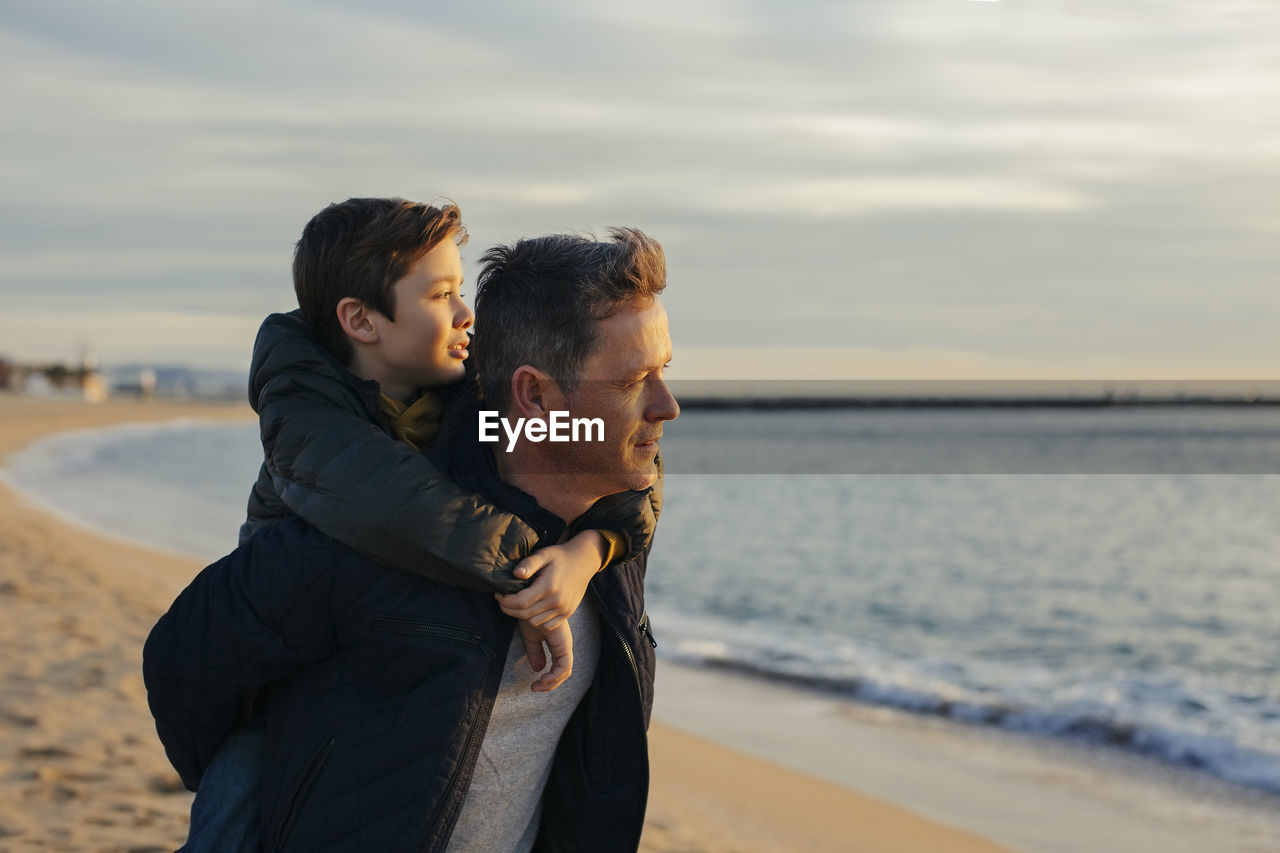 Father carrying son piggyback on the beach