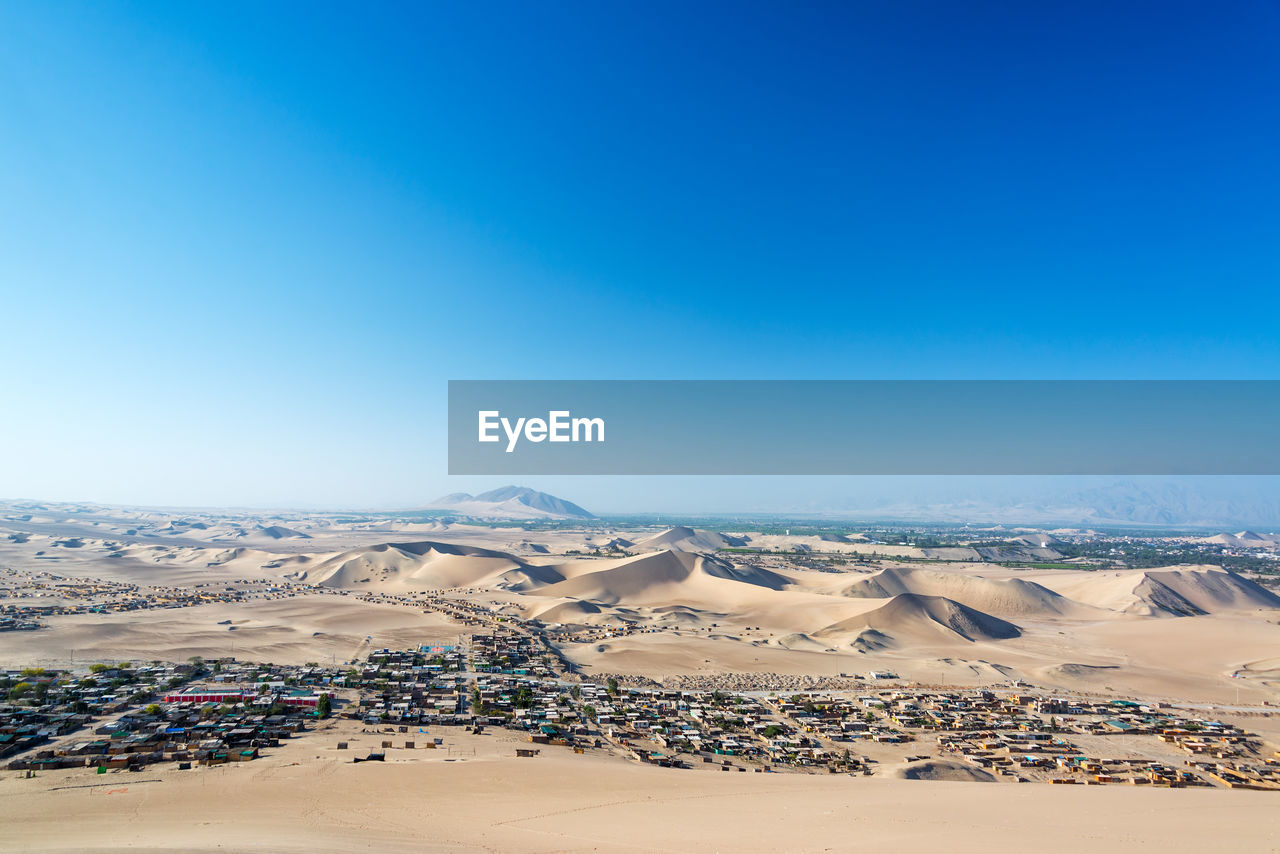 Scenic view of desert landscape against clear blue sky at huacachina