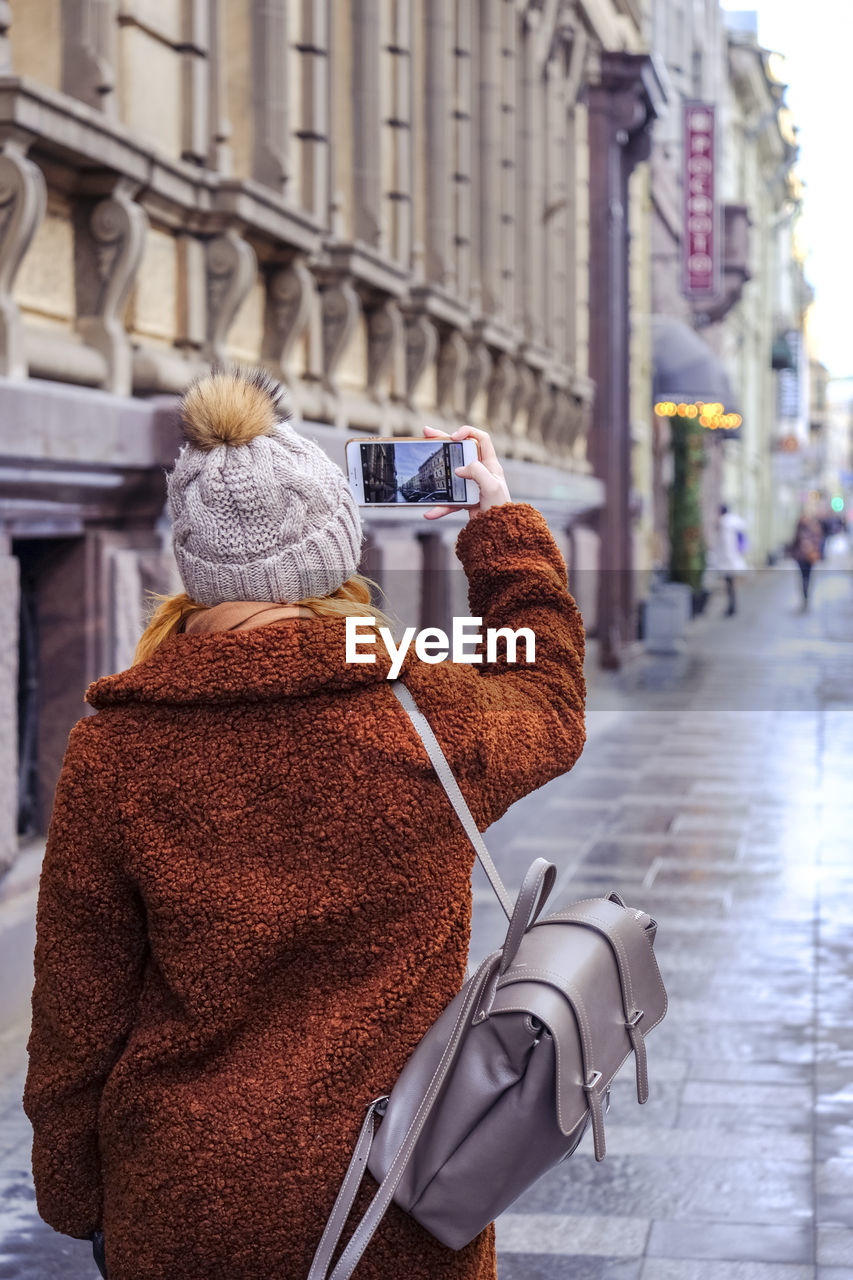 Rear view of woman photographing on footpath in city