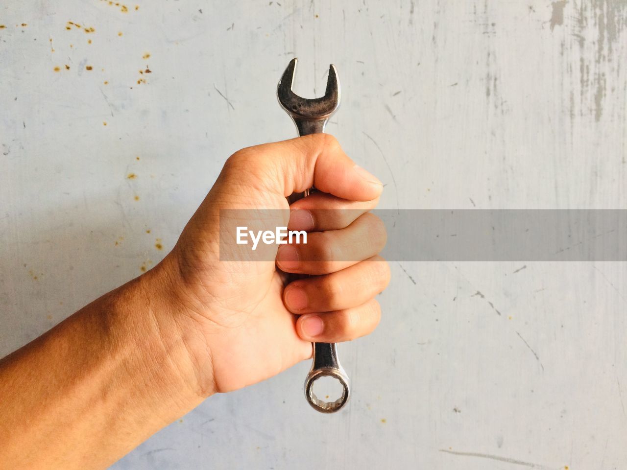 Cropped hand of person holding wrench against wall