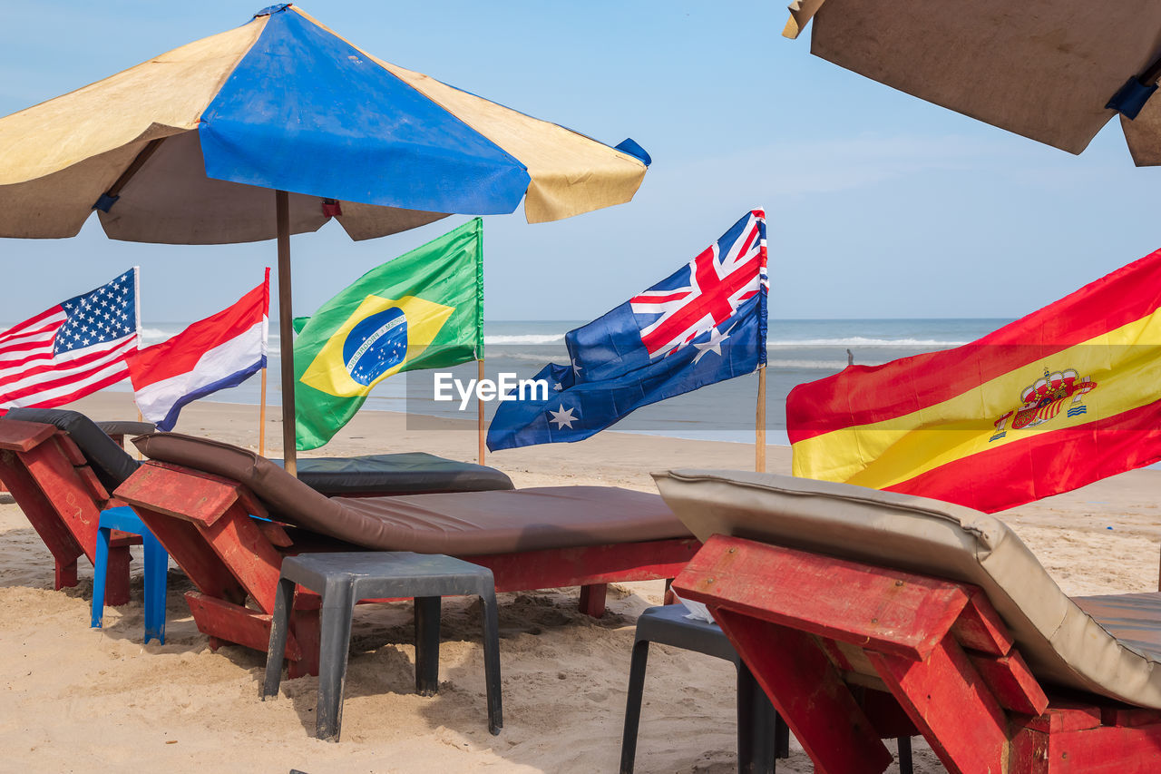 Flags from different countries on the beach with empty sunbeds waiting for new tourists.