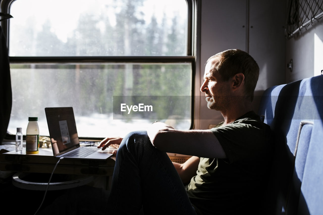 Businessman using laptop while sitting by window in train