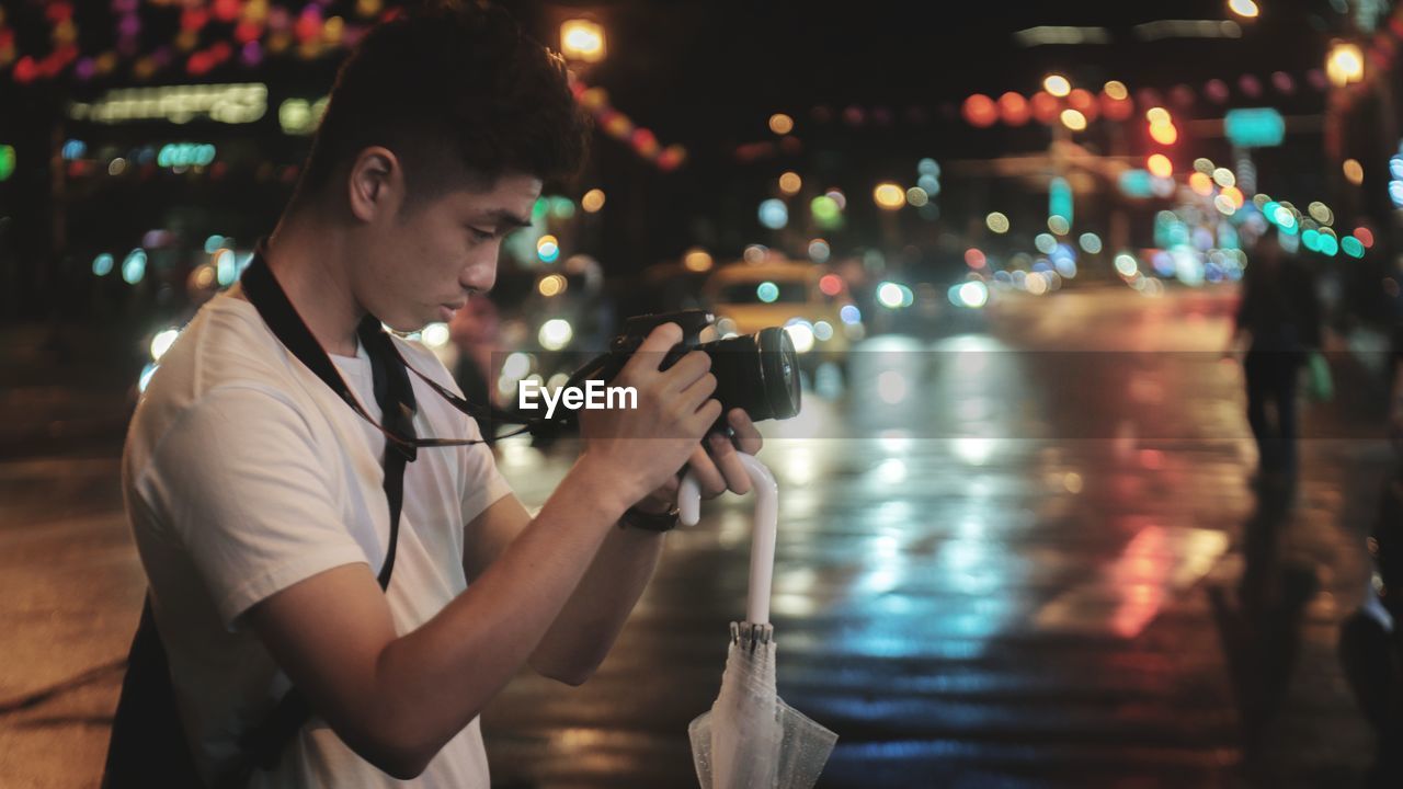 Side view of young man photographing in city at night