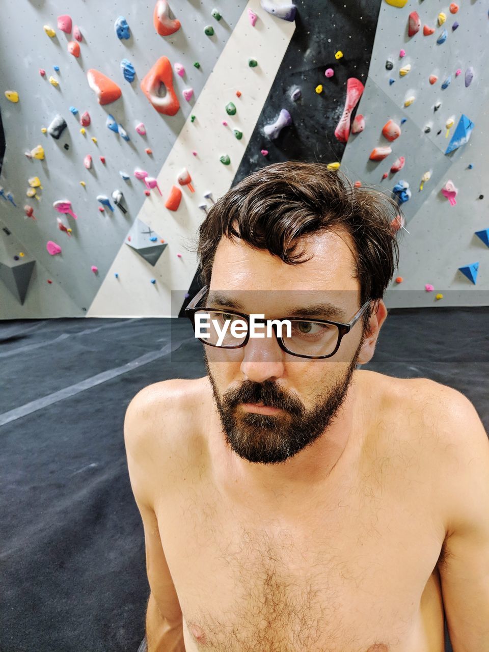 Shirtless man sitting against climbing wall