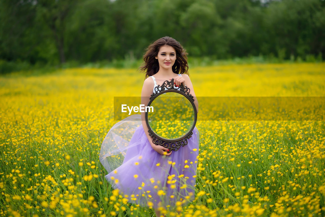 Portrait of woman with yellow flower on field