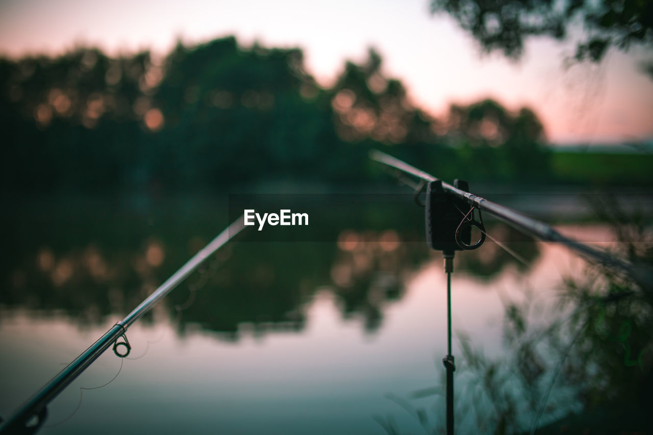 Close-up of fishing rods by lake during sunset