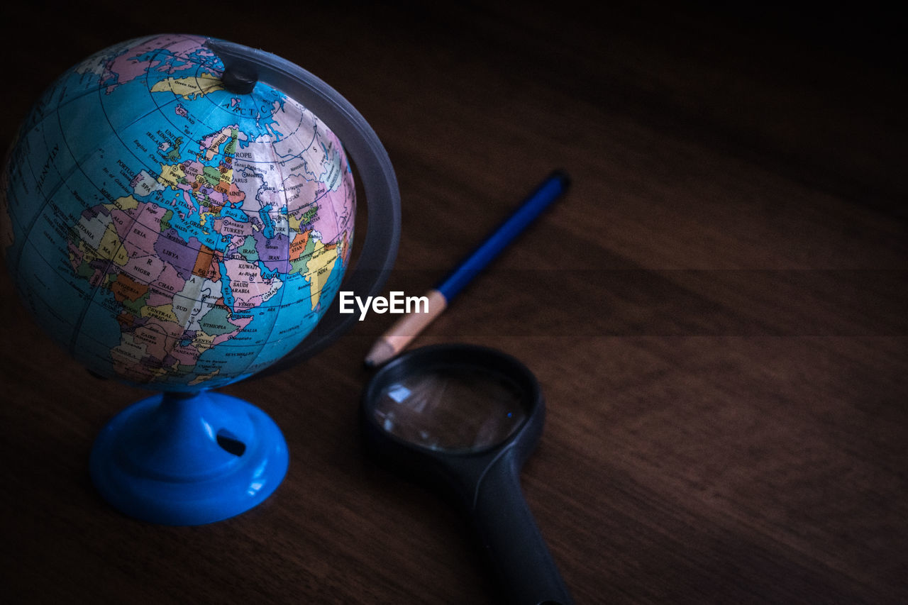 High angle view of globe with pencil and magnifying glass on table