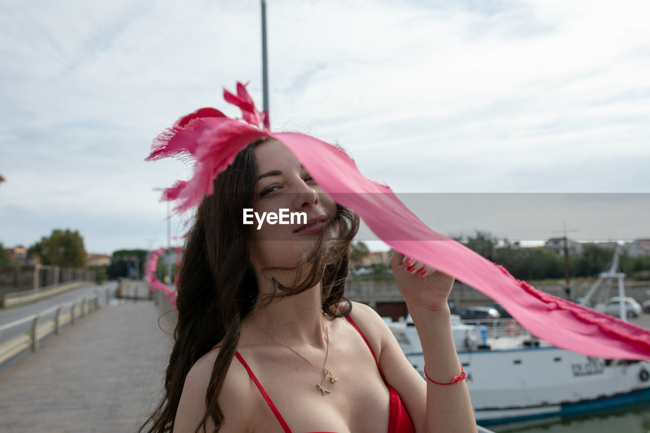 Portrait of smiling woman standing by pink flag at harbor