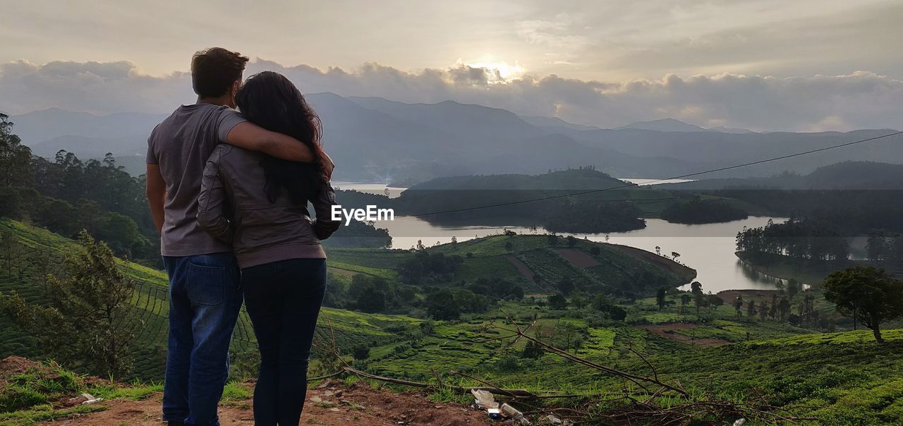 Rear view of couple standing against mountains and river