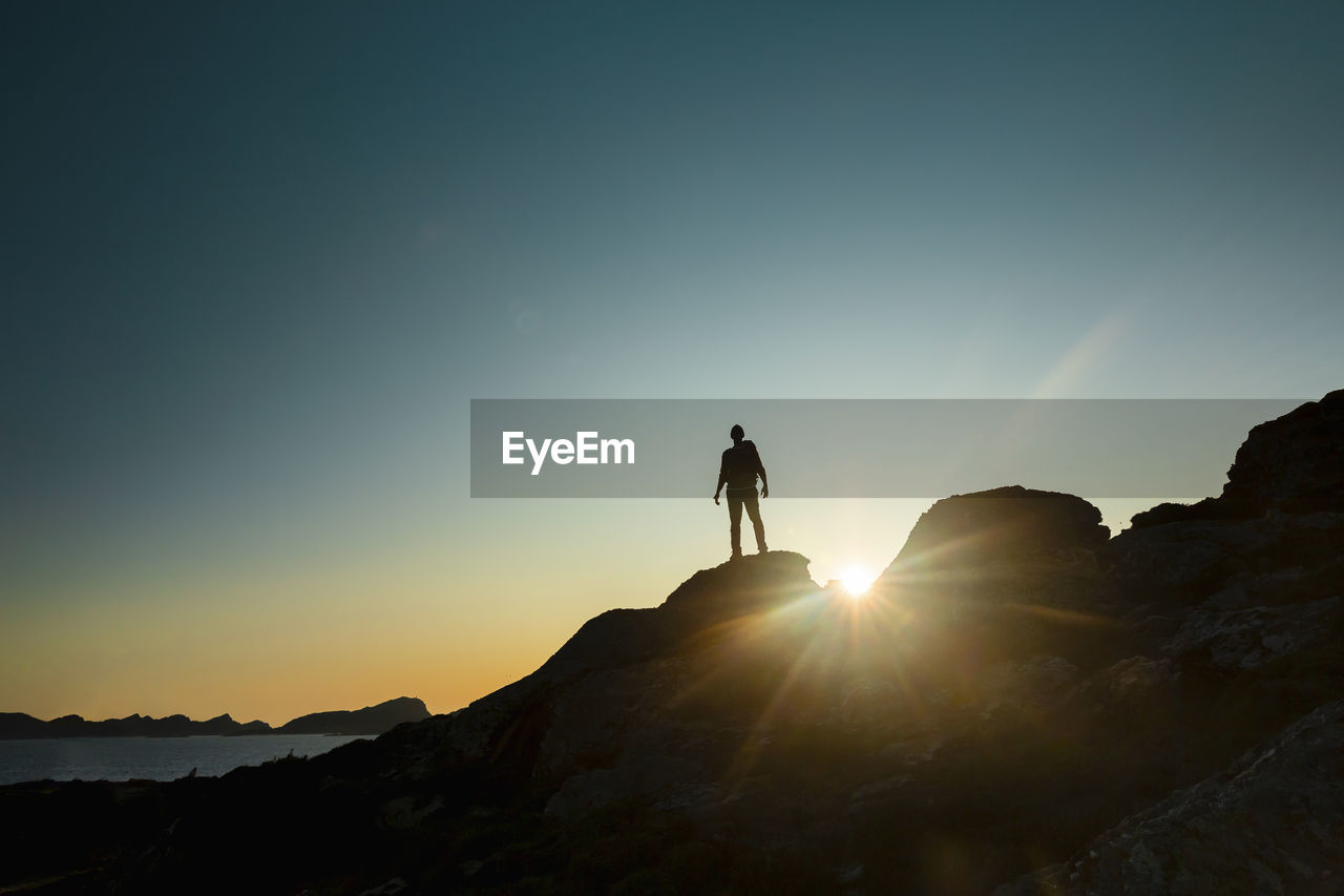 Man silhouette over a rock at sunset