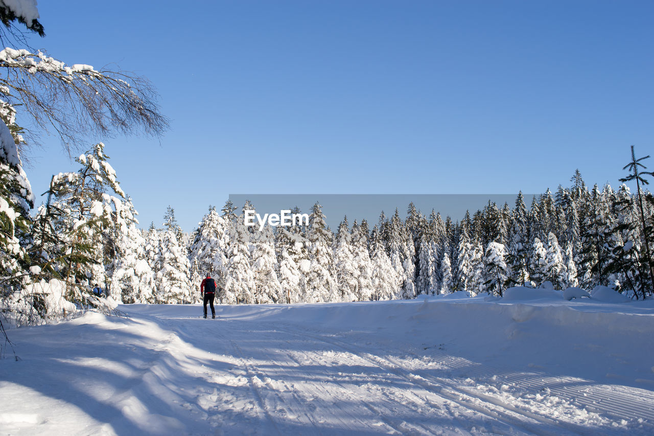 Man skiing on snow covered field against clear sky