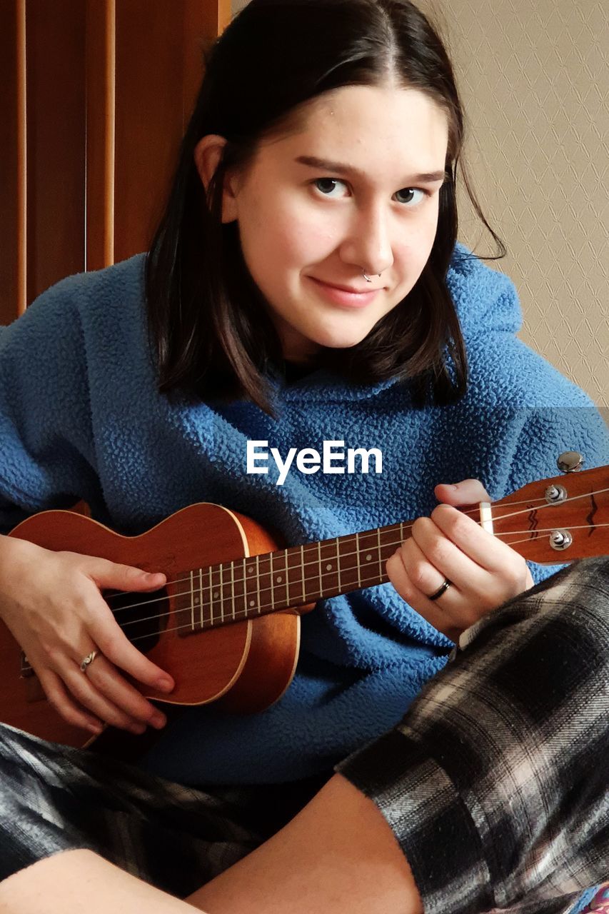 Portrait of a young girl with an earring in her nose playing the ukulele