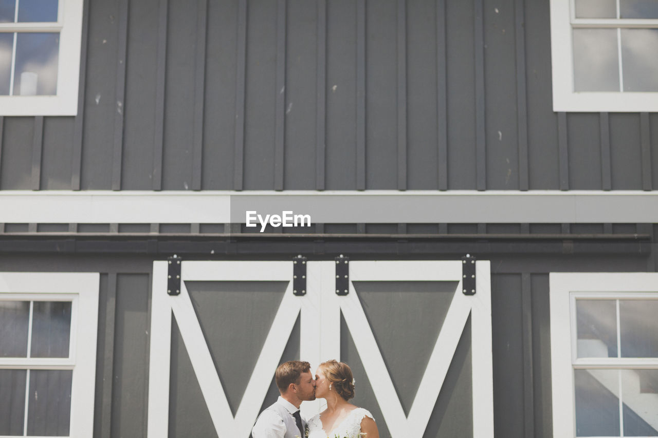 Newlywed young couple kissing against building