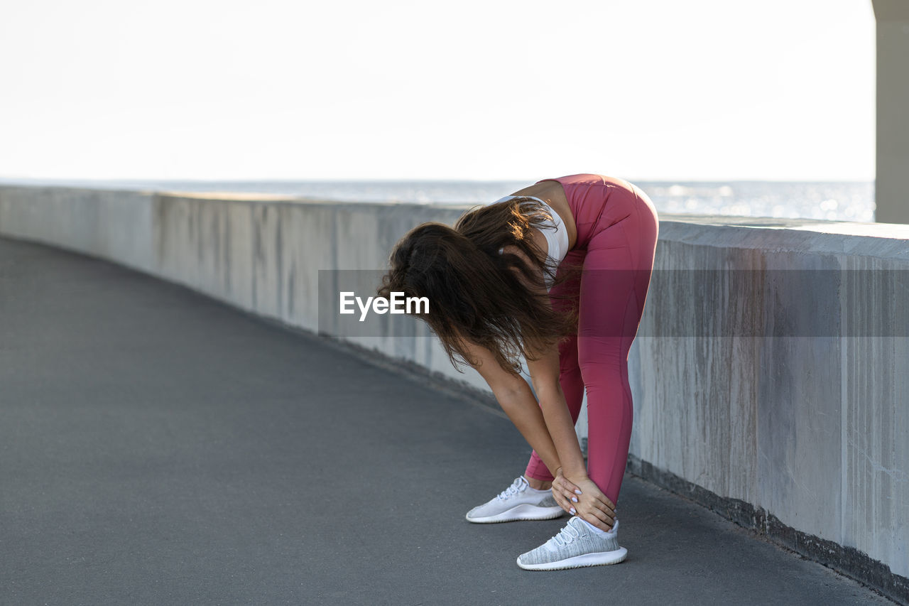 Full length of woman exercising while standing against bridge