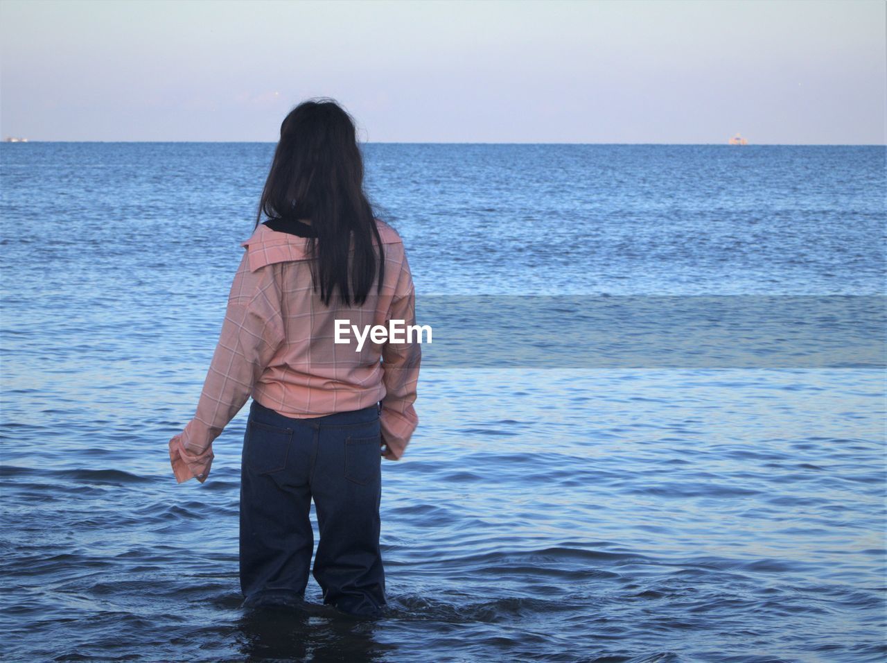 Rear view of young woman standing in sea against sky