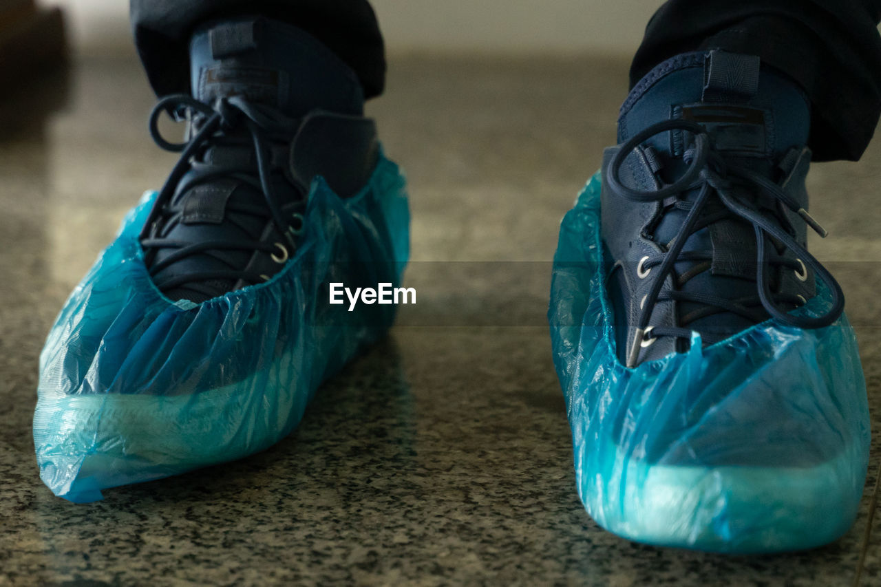 Low section of man wearing plastic on shoe