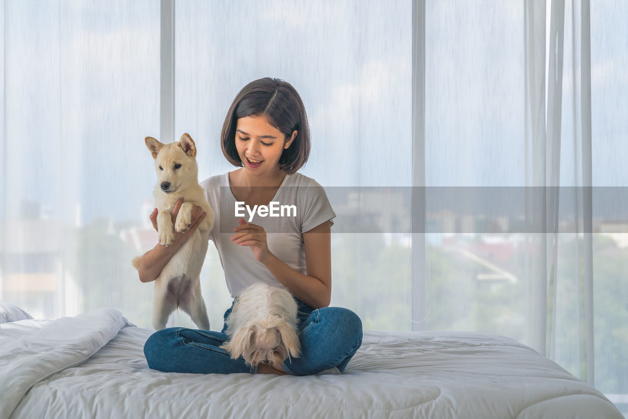 YOUNG WOMAN WITH DOG SITTING ON BED