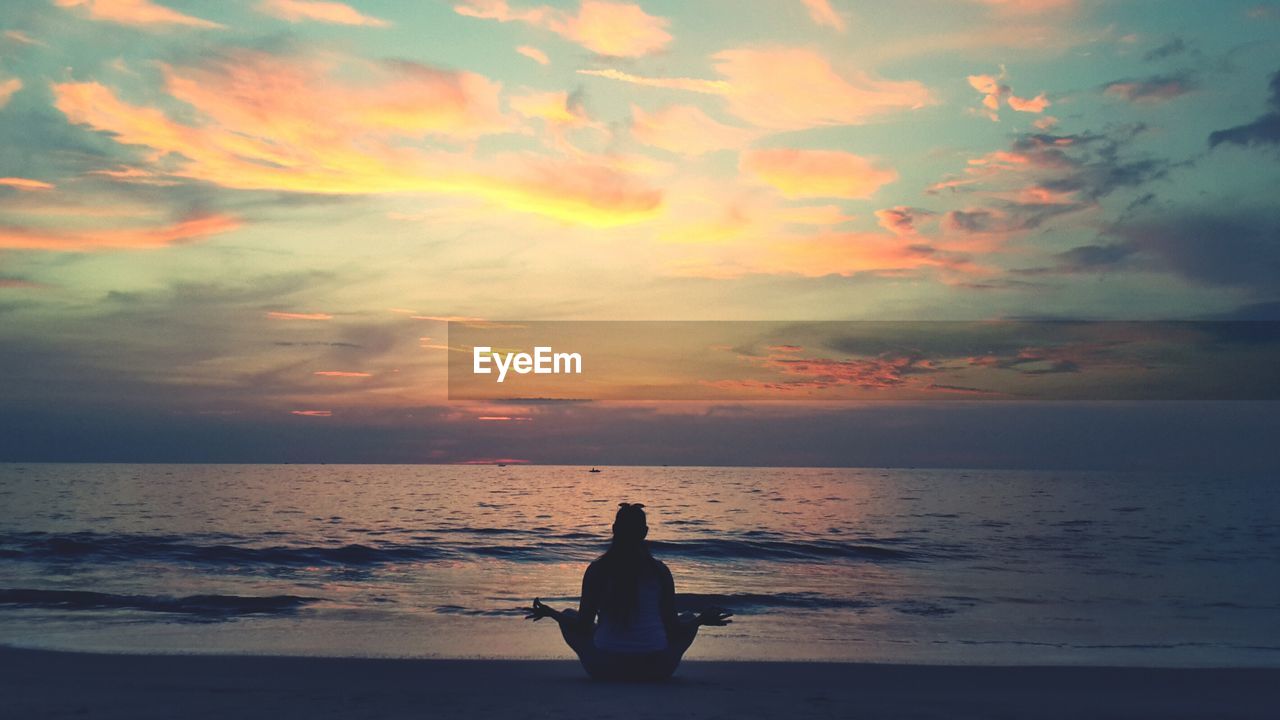 Silhouette woman relaxing at beach against sky during sunset