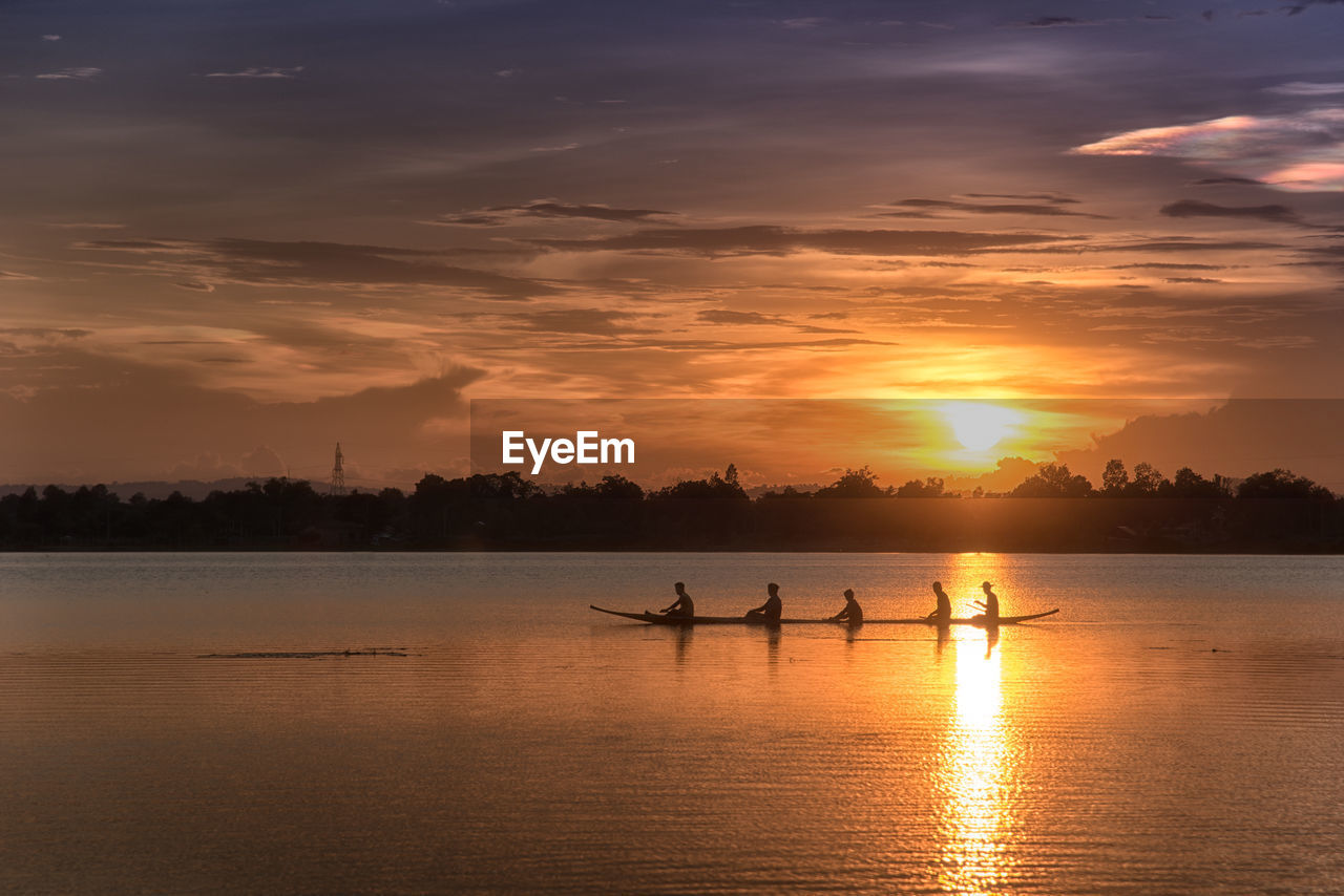 Side view of silhouette people rowing rowboat in lake against sky during sunset