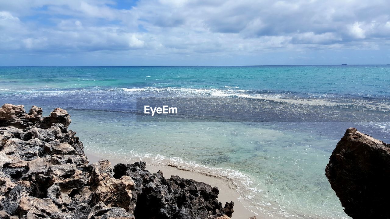 View of calm beach against cloudy sky