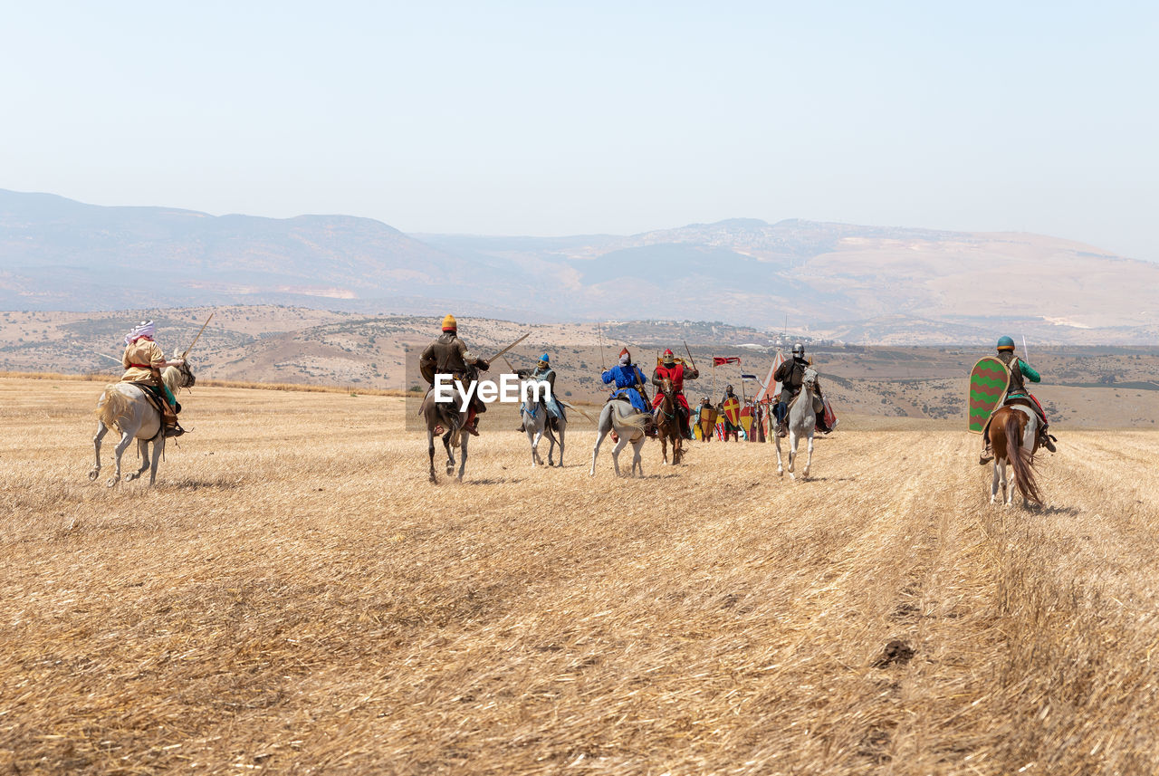 GROUP OF PEOPLE RIDING HORSES ON LANDSCAPE