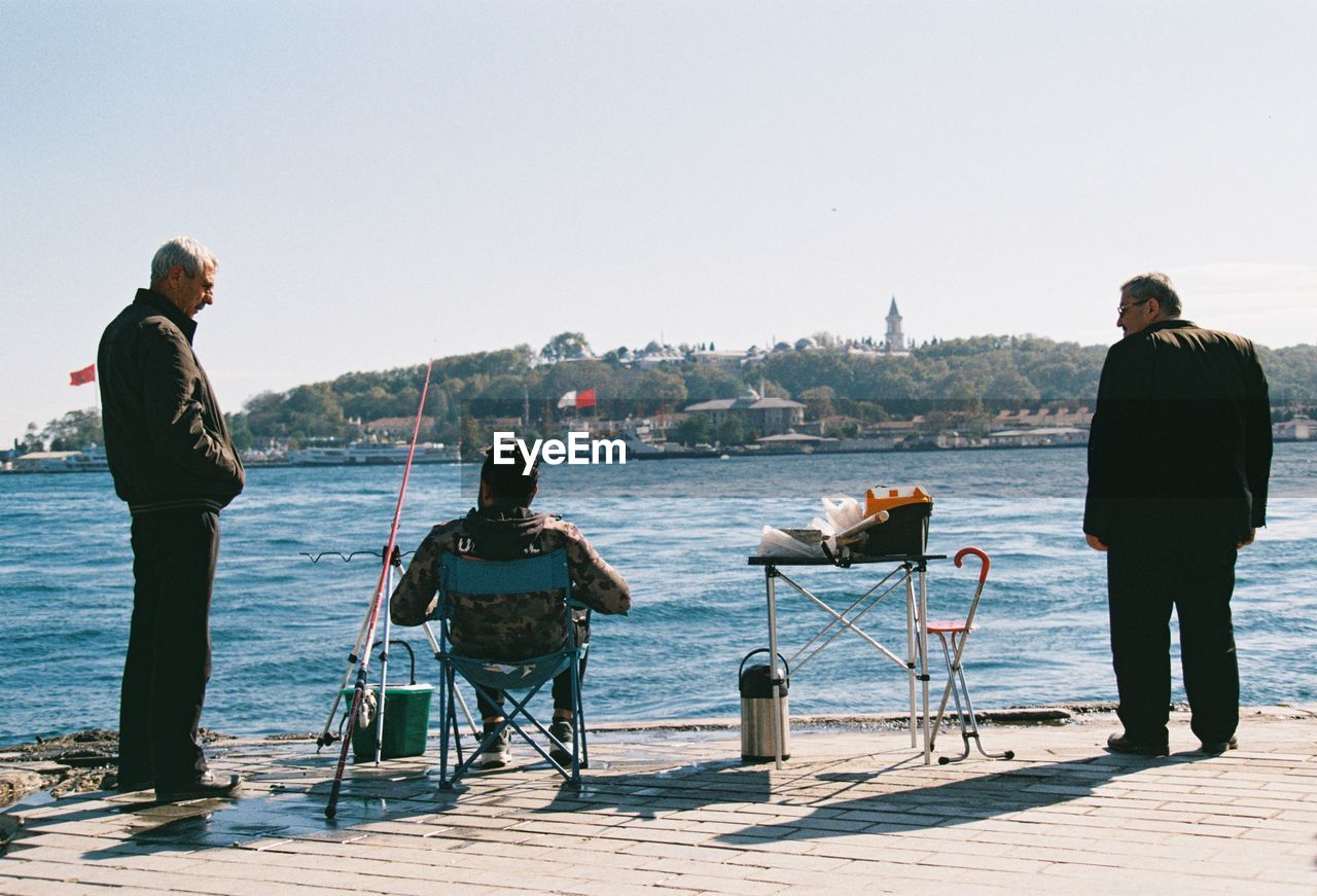 Rear view of men standing by sea against clear sky
