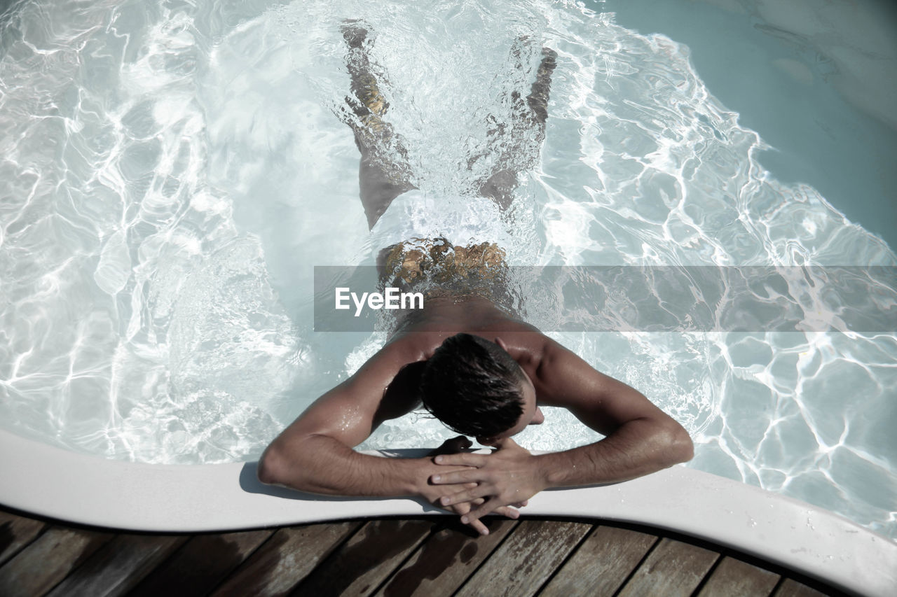 Rear view of young man relaxing in swimming pool