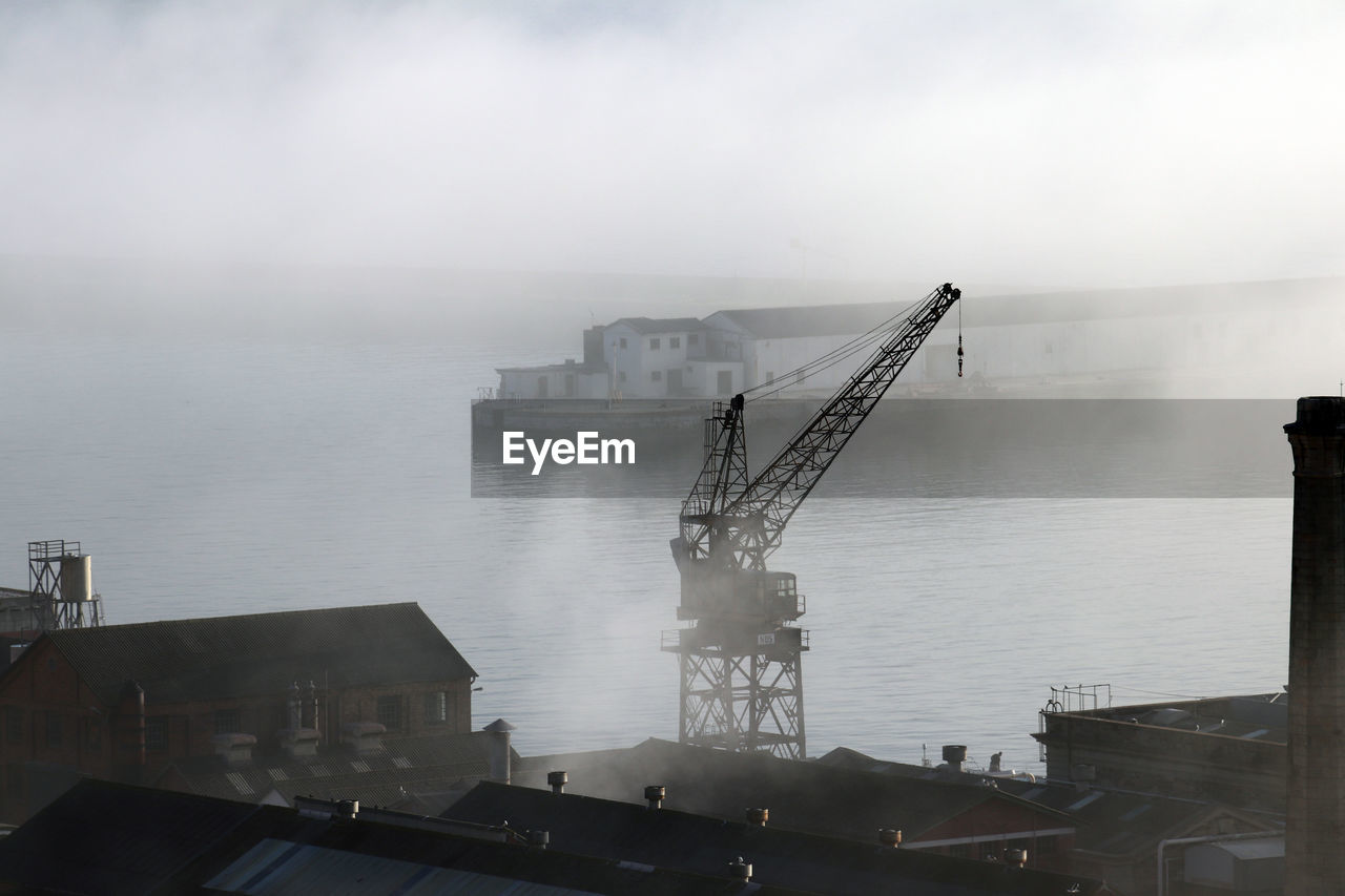 CRANES AT PIER BY SEA AGAINST SKY