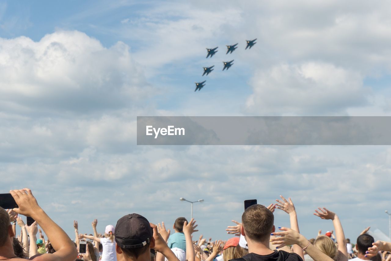 Low angle view of people watching airshow against sky