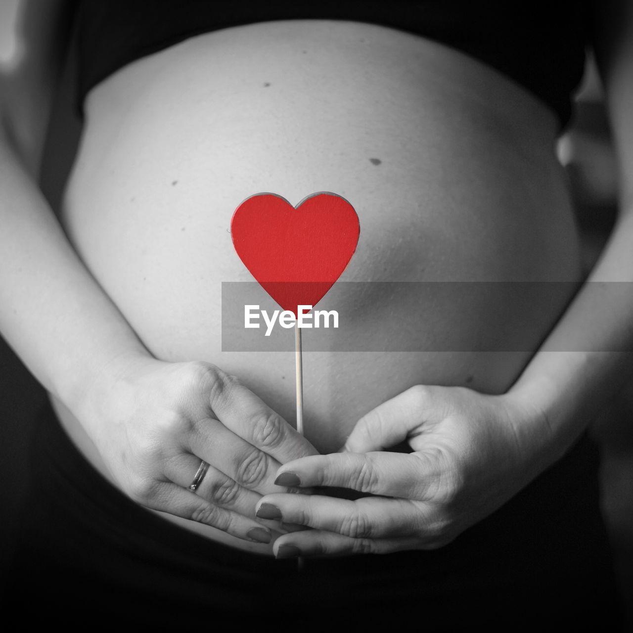 Midsection of pregnant woman holding heart shape at home