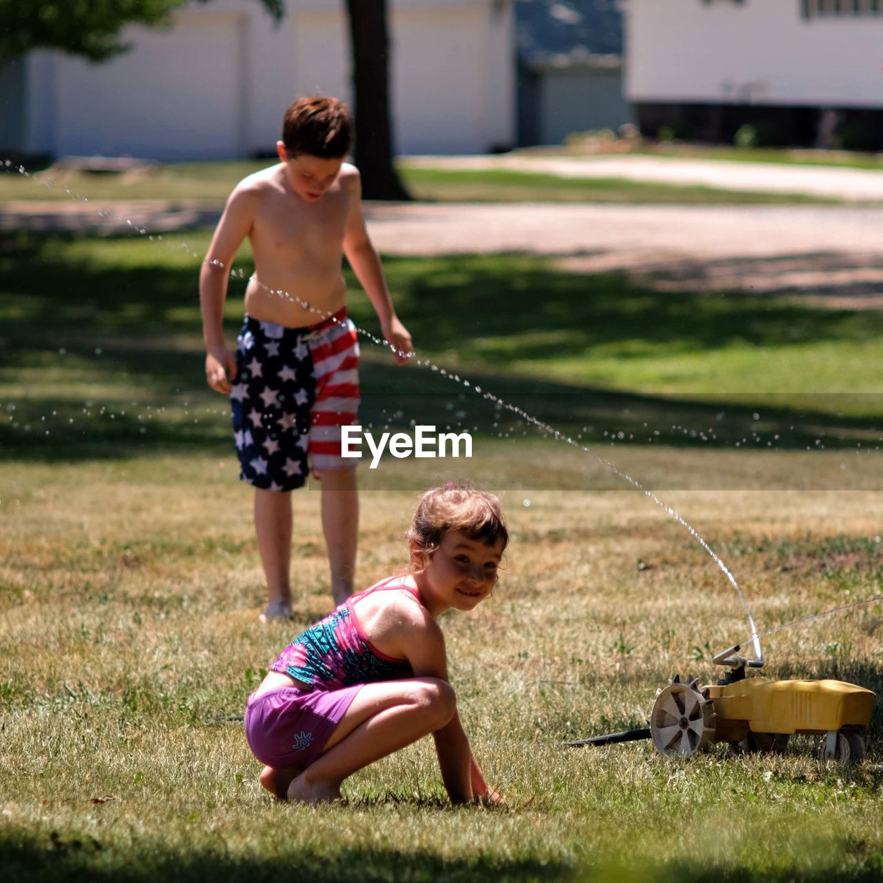 Water spraying on shirtless boy with sister in yard