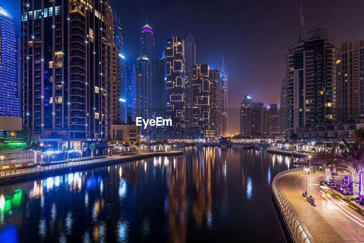 Night city dubai in uae. illuminated buildings by river against sky in city at night