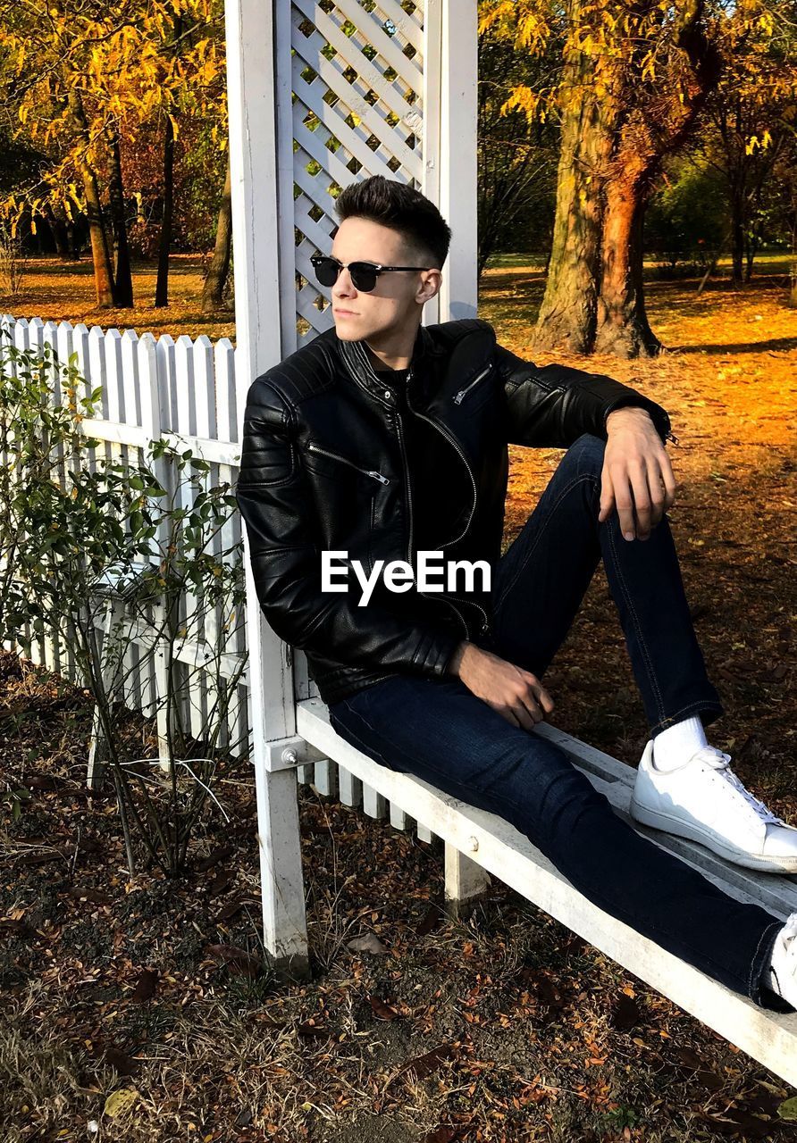 Fashionable young man looking away while sitting on bench in park