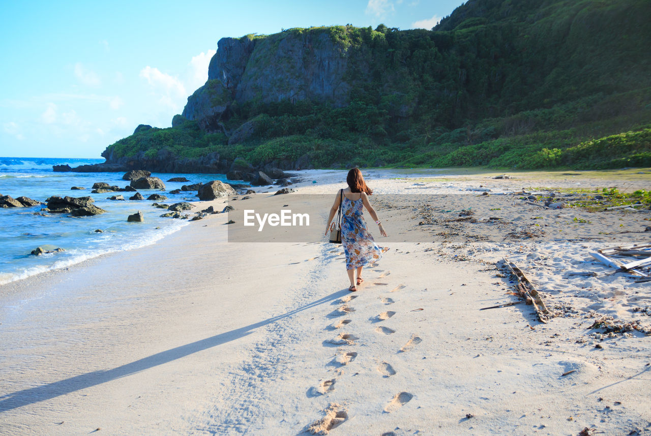 Rear view of woman walking at beach against sky