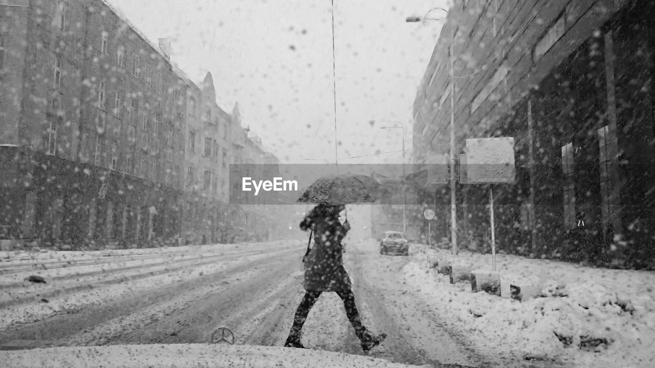 Side view of mid adult woman walking on road during snowfall seen through windshield