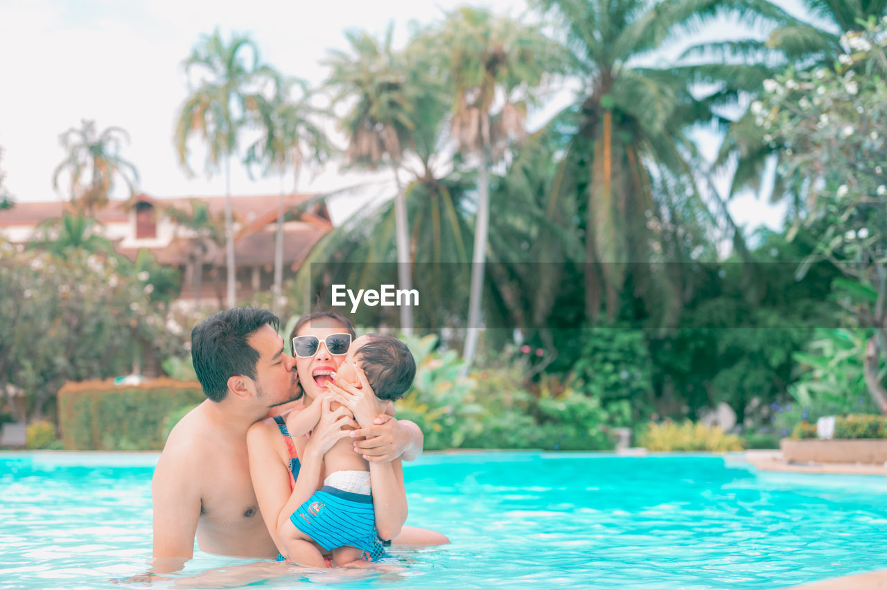 FATHER AND DAUGHTER IN SWIMMING POOL AGAINST TREES AT PARK