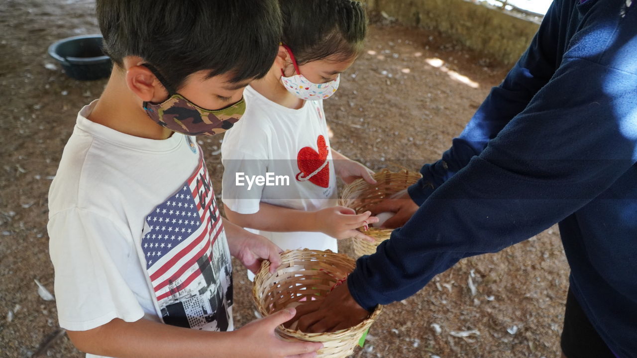 High angle view of siblings wearing masks giving wicker baskets to man